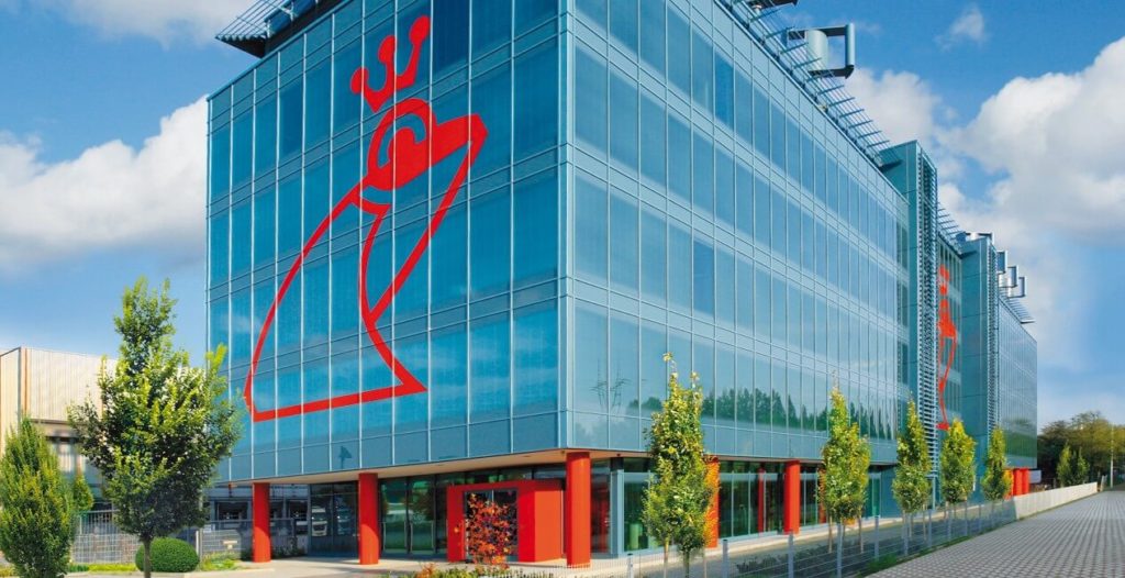 Photo d'un des bâtiments modernes de l'entreprise Werner & Mertz en Allemagne. On peut y voir son logo en forme de grenouille rouge apposé sur les vitres. 